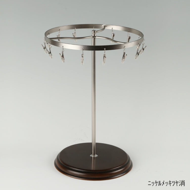 ●商品名:チーフ・ハンカチスタンド回転式 木製ベース仕様
●表面処理:ニッケルツヤ消(NI-M)仕上
●寸法:高さ315mm 上部回転リング直径240mm
●上部回転式リング:クリップ15個付
●材質:スチール
●特長:百貨店様では棚板高さのスパンが30cm強の設定が多いと教えてもらい、では「高さ30cmのスペースにフィットするチーフツリーを作ろう」ということで高さ30cmのチーフツリーを製造しました。また、クリップの先端には塩ビのキャップを装着し、展示商品を傷つけにくい仕上がりになっています。さらに、木製のベースを組み合わせることで、落ち着きのある存在感と高級感を演出できます。
●生産国:日本(タヤ自社工場)